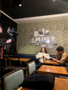 Une image représentant un étudiant de l'atelier en train de filmer deux autres étudiant.e.s dans un coffee shop.