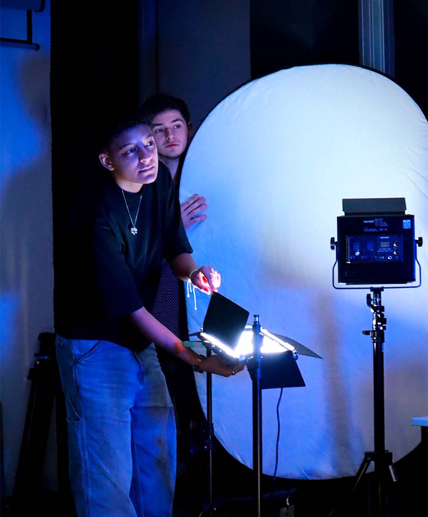 Vue d’ensemble d’une pièce avec deux étudiants, un tenant un éclairage et l’autre un fond blanc.