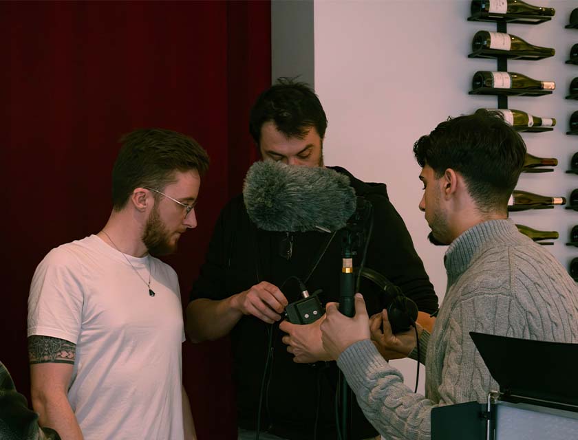 Vue de face de deux étudiants et d’un intervenant ; l’intervenant tient une caméra, ainsi que l’un des deux étudiants