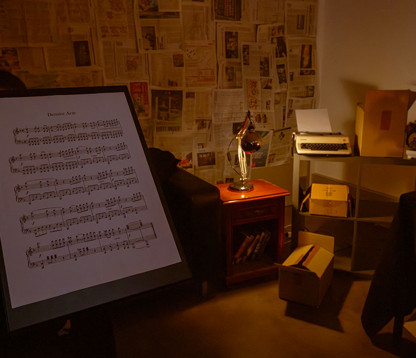 Vue d’ensemble d’une pièce mise en scène pour l’atelier vidéo, avec un canapé, une table avec une lampe, une affiche avec des notes de musique, ainsi qu’un meuble.