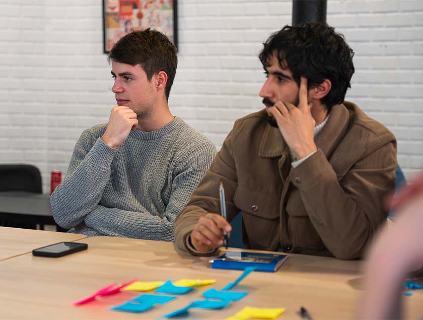 Vue sur deux étudiants assis sur des chaises, avec une table sur laquelle sont posés des post-it.