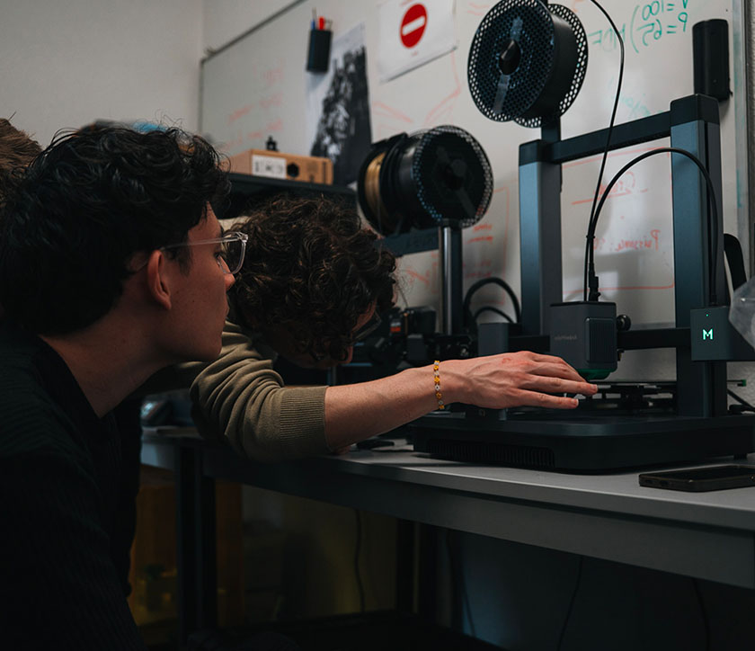 Vue sur deux étudiants, l'un est en train de régler un appareil 3D et l’autre regarde l’appareil.