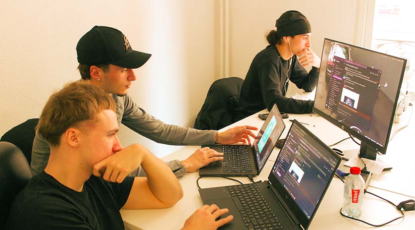 Vue sur une salle avec trois étudiants, chacun en train de travailler sur son ordinateur.