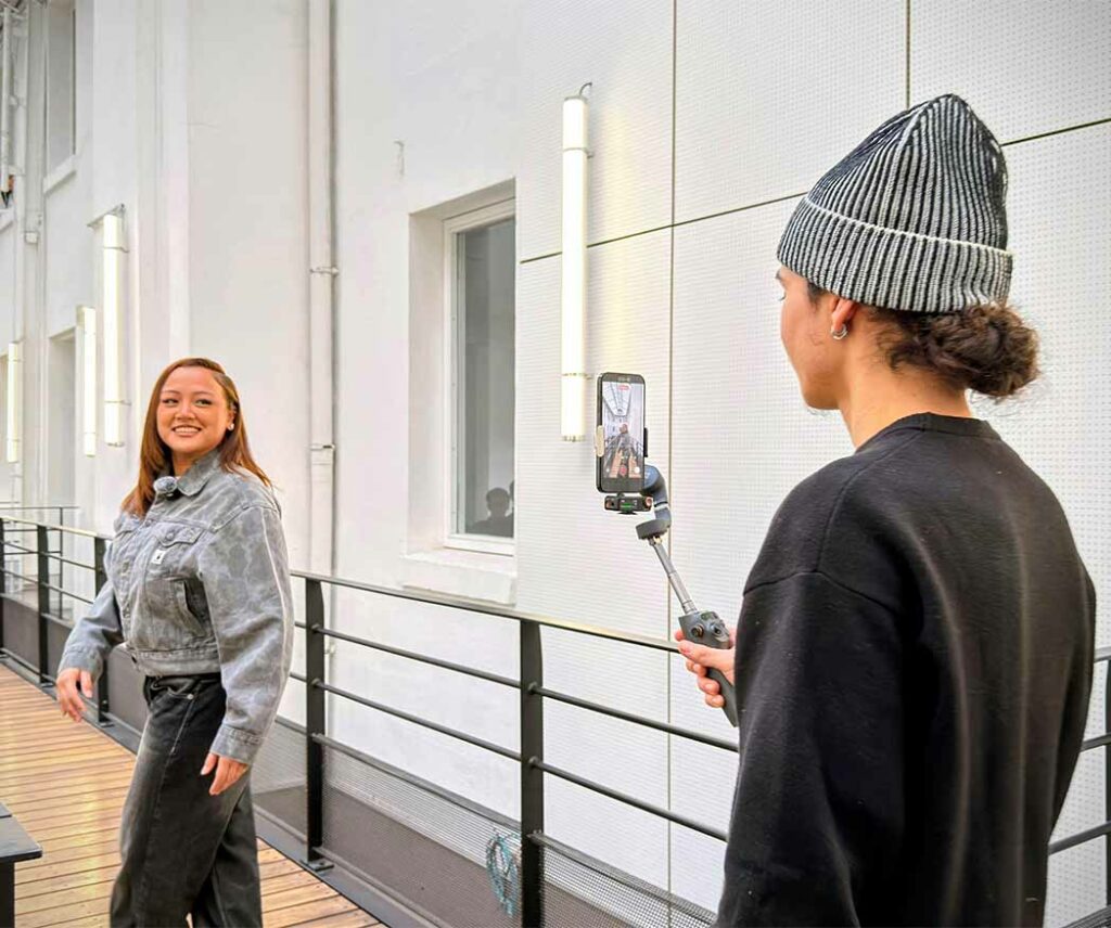Vue sur un étudiant qui prend une vidéo avec son téléphone d’une étudiante sur la passerelle de l’école.